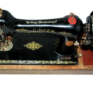 May include: A vintage Singer sewing machine, black with gold accents, mounted on a wooden base. The machine features the Singer Manufacturing Co. logo and decorative floral patterns. The hand wheel is visible on the right side.