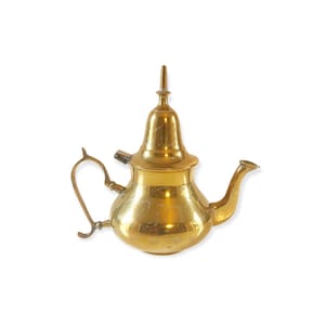 Może przedstawiać: Złoty metalowy czajnik z zakrzywionym dziobkiem i uchwytem. Czajnik ma ozdobny wzór z wytrawionymi wzorami i wysoką, spiczastą pokrywką. Prawdopodobnie służy do serwowania herbaty i ma klasyczną, vintage estetykę.