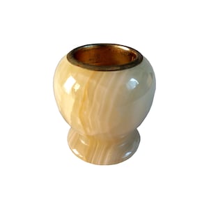 Könnte beinhalten: Ein kleiner, runder Behälter aus cremefarbenem Onyx. Er hat einen goldfarbenen Rand und einen Sockel. Der Onyx weist eine natürliche, marmorierte Optik auf. Der Behälter dient wahrscheinlich zur Aufbewahrung kleiner Gegenstände oder als dekoratives Element.