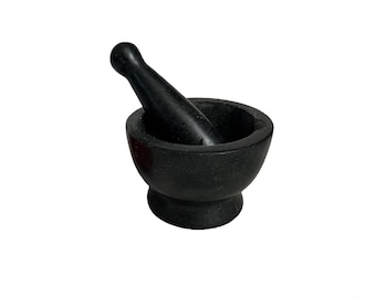 May include: A black mortar and pestle set. The mortar is a bowl-shaped vessel with a rounded base. The pestle is a cylindrical tool with a rounded handle. Both pieces are made of a dark, possibly stone material.