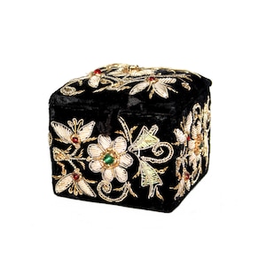 May include: A black velvet box with detailed floral embroidery. The flowers are white with gold detailing and feature red and green gemstone centres. The box is square and has a hinged lid.