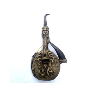 Könnte beinhalten: Ein handgefertigtes, beige-farbenes, gourd-förmiges Gefäß mit aufwendigen Schnitzereien. Das Design umfasst ein bärtiges Gesicht, dekorative Muster und einen gebogenen Ausguss. Ein Horn und ein knochenfarbenes Rohr sind befestigt.