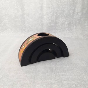 K&ouml;nnte beinhalten: Schwarzes Holzdekor in Regenbogenform mit floralem Design in Rosa, Gelb und Gr&uuml;n. Der Artikel hat oben ein Loch und besteht aus drei gestapelten B&ouml;gen.