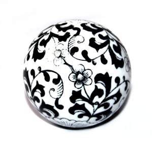 May include: A white, spherical decorative object with a black floral pattern. The design features stylized flowers and leaves, creating a contrasting aesthetic. The object is set against a plain white background.