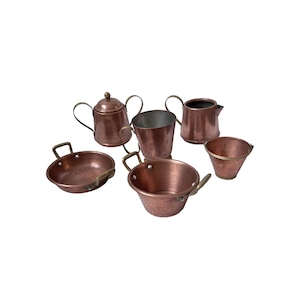 May include: A set of miniature copper kitchen utensils, including a teapot, a jug, a saucepan, a bucket, and two other containers. The copper items have brass handles and rims. The items are arranged on a white background.
