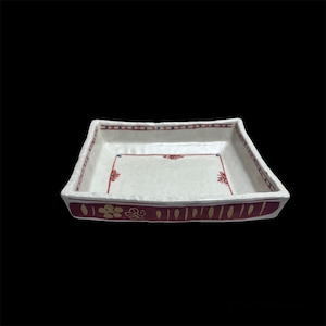 Könnte beinhalten: Quadratische Keramikschale mit weißem Innenraum und burgunderfarbenem Rand. Der Rand ist mit goldenen Blumen- und vertikalen Liniendesigns verziert. Der Rand hat ein rot-blaues Muster. Die Schale hat eine leicht strukturierte Oberfläche.