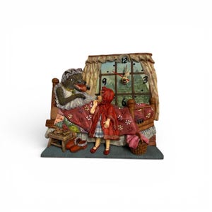 May include: A decorative clock depicting a scene from Little Red Riding Hood. The wolf is in bed, and Red Riding Hood stands before him. The clock face is visible in the window. The scene is set on a blue base.