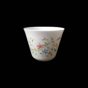 May include: White ceramic bowl with a flared shape, decorated with a floral pattern. The design features pink, blue, and yellow flowers with green vines. The bowl has a smooth, glossy finish.