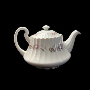 Peut inclure: Théière en porcelaine blanche avec couvercle, ornée de roses roses et vertes. La théière a une anse et un bec courbés, avec une bordure dorée sur le bord et le couvercle. Fond noir.