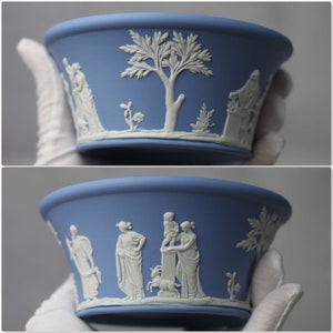 May include: A light blue ceramic bowl with white bas-relief classical figures and a tree design. The bowl has a wide rim and a slightly flared shape. The white relief details contrast with the blue background.