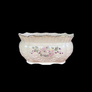May include: Cream ceramic planter with a scalloped rim and floral design. The planter has a pink and purple floral pattern in the centre, with embossed detailing along the base. The rim is trimmed with gold.