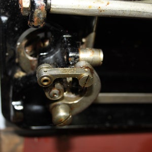 May include: Close-up of a vintage sewing machine mechanism. The image shows a detailed view of the machine's internal components, including metal parts with signs of age and wear. The focus is on the intricate mechanical details.