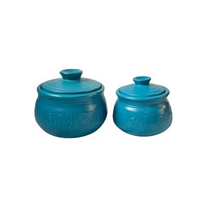 May include: Two turquoise ceramic lidded jars. The jars have a round shape with embossed floral designs and a matching lid with a knob. The jars are a matching set and are a vibrant teal colour.