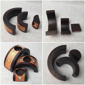 K&ouml;nnte beinhalten: Eine Sammlung dunkelbrauner Kerzenhalter aus Holz in verschiedenen Gr&ouml;&szlig;en und Formen. Einige haben ein dekoratives Band mit floralen Mustern in Orange, Gold und Wei&szlig;. Die Kerzenhalter sind auf einer hellgrauen Oberfl&auml;che angeordnet.