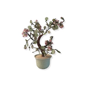 May include: A decorative bonsai tree in a pale blue ceramic pot. The tree has a brown trunk, green leaves, and pink flower blossoms. The pot is filled with small white pebbles.