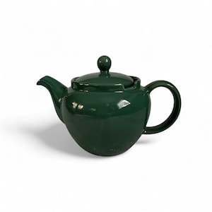 May include: A glossy, emerald green ceramic teapot with a matching lid and a rounded handle. The teapot has a curved spout and a spherical body. The lid features a small, round knob. The teapot is designed for brewing tea.
