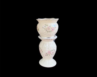 May include: A two-piece ceramic vessel set featuring a cream-colored base with an embossed scrollwork texture. Both pieces are decorated with a floral pattern of pink and purple flowers with green leaves and finished with a thin gold-toned rim.