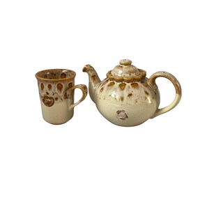 May include: A ceramic teapot and matching mug featuring a cream-colored base with brown drip-style glaze accents around the rims and lids. Both pieces display a circular logo with the text "HORNSEA POTTERY" printed on the side of the items.