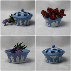 May include: A collection of four images showcasing a blue ceramic flower frog with a lid. The frog features white relief designs of figures and trees. Some images show the frog filled with flowers.