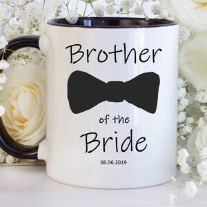 Pu&ograve; includere: Tazza in ceramica bianca con interno e manico neri. La tazza presenta la scritta "Brother of the Bride" con un papillon nero e la data 06.06.2019. La tazza &egrave; circondata da fiori bianchi.