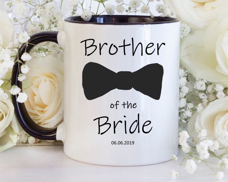 Pu&ograve; includere: Tazza in ceramica bianca con interno e manico neri. La tazza presenta la scritta "Brother of the Bride" con un papillon nero e la data 06.06.2019. La tazza &egrave; circondata da fiori bianchi.