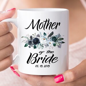 May include: White ceramic mug with a black floral design and the text "Mother of the Bride 05.19.2019".