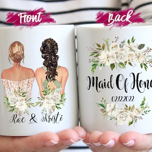 May include: White ceramic mug featuring illustrations of two women in dresses, with floral accents. The front of the mug has the names "Rae & Kristi". The back of the mug says "Maid Of Honor" and the date "02.12.2022".