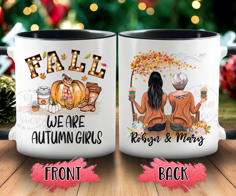 May include: White ceramic mug with a black interior and handle. The front features the word "FALL" in illuminated letters, a pumpkin, and the text "WE ARE AUTUMN GIRLS." The back shows two women with coffee, the names "Robyn & Mary", and fall foliage.