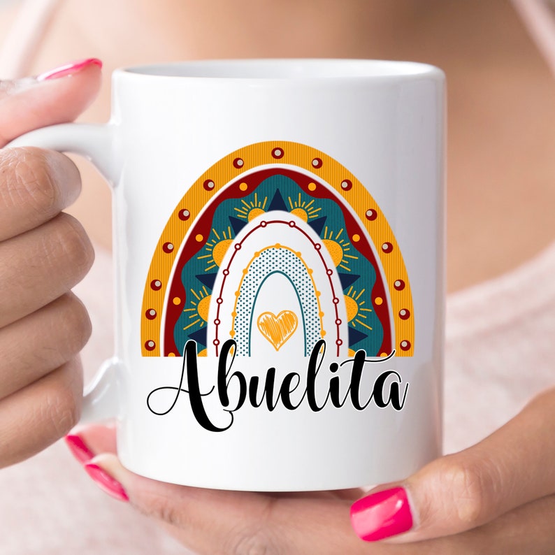 May include: White ceramic mug featuring a colorful rainbow design with a heart and the word "Abuelita" in black script. The rainbow includes shades of yellow, teal, and red. A perfect gift for a grandmother.