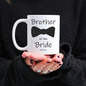 Pu&ograve; includere: Tazza in ceramica bianca con la scritta "Brother of the Bride" e un'immagine di papillon nero. La data "06.06.2019" &egrave; stampata sotto. La tazza ha un manico curvo.