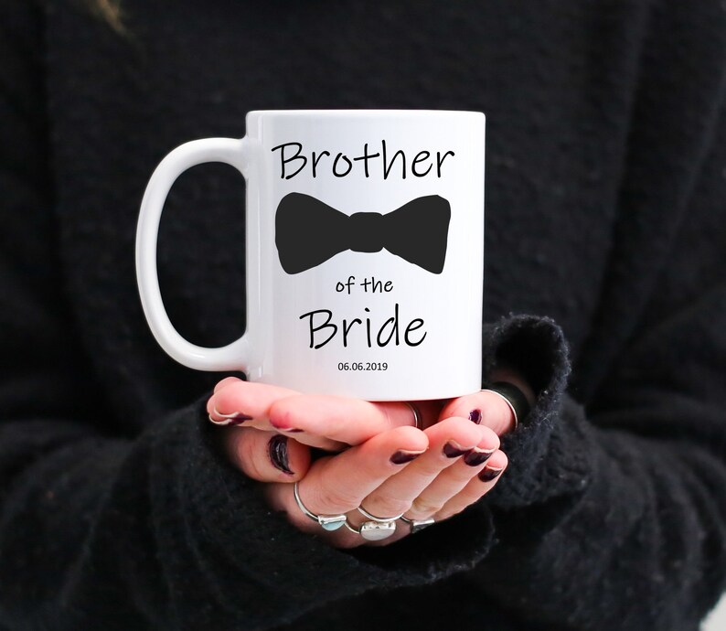 Pu&ograve; includere: Tazza in ceramica bianca con la scritta "Brother of the Bride" e un'immagine di papillon nero. La data "06.06.2019" &egrave; stampata sotto. La tazza ha un manico curvo.