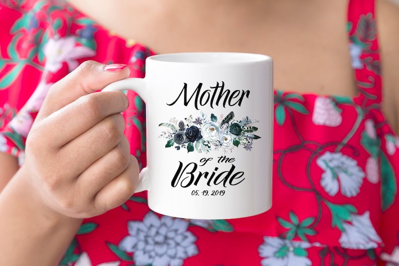 May include: White ceramic mug with a black floral design and the text "Mother of the Bride" with the date "05.19.2019".