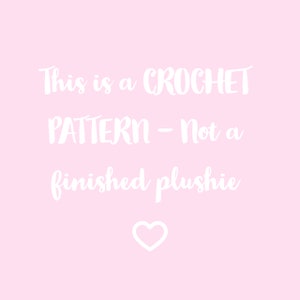 May include: A pink background with white text that reads "This is a CROCHET PATTERN - Not a finished plushie" with a white heart at the bottom.