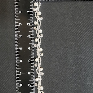 May include: A silver and white beaded trim with small pearls and rhinestones. The trim is measured against a ruler, showing it is approximately 7 inches long.