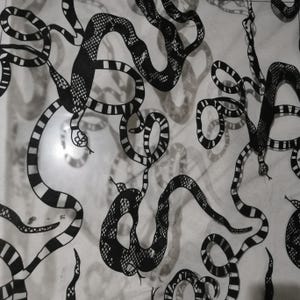 Könnte beinhalten: Schwarzes und weißes Schlangenmuster. Das Design zeigt zahlreiche Schlangen in verschiedenen Posen mit detaillierten Schuppen und Streifenmustern. Die Schlangen sind vor einem hellen Hintergrund platziert und erzeugen einen hohen Kontrast.