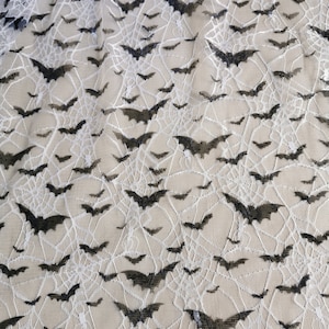 May include: Black bats and white spiderwebs on a beige mesh fabric. The fabric is sheer and has a delicate texture.