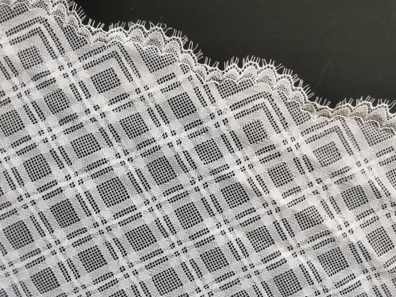 May include: White lace fabric with a square pattern. The lace has a scalloped edge.
