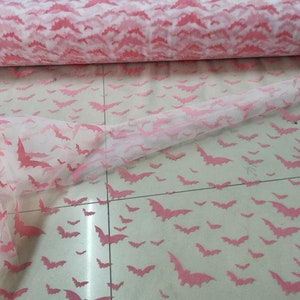 Op de afbeelding: Roze tule stof met een herhalend patroon van roze vleermuizen. De stof is doorschijnend en lichtgewicht.