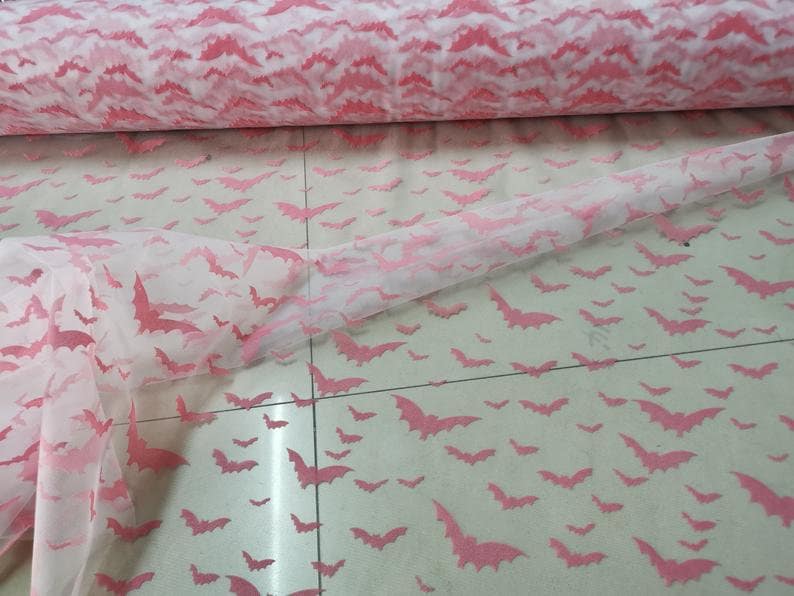 Op de afbeelding: Roze tule stof met een herhalend patroon van roze vleermuizen. De stof is doorschijnend en lichtgewicht.