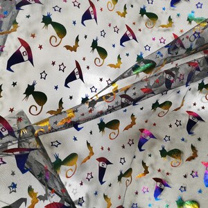 K&ouml;nnte beinhalten: Schwarzer T&uuml;llstoff mit einem regenbogenfarbenen, schimmernden Druck von Sternen, Flederm&auml;usen, Katzen und Hexenh&uuml;ten.