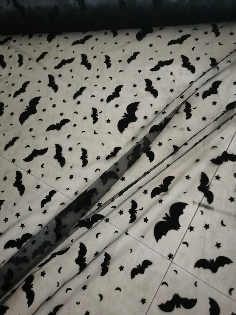 May include: Black sheer fabric with a repeating pattern of bats and stars. The fabric is folded in half, showing the pattern on both sides.
