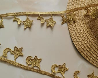 Peut inclure: Garniture dorée avec un motif répété d'étoiles et de croissants de lune. La garniture est faite d'un matériau délicat et de type dentelle.