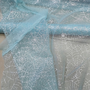 Peut inclure: Un rouleau de tissu tulle bleu clair avec des toiles d'araign&eacute;es argent&eacute;es &agrave; paillettes imprim&eacute;es dessus.
