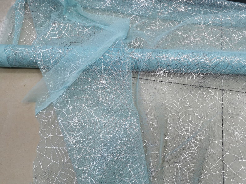 Peut inclure: Un rouleau de tissu tulle bleu clair avec des toiles d'araign&eacute;es argent&eacute;es &agrave; paillettes imprim&eacute;es dessus.