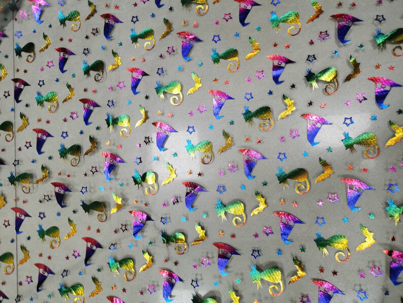 K&ouml;nnte beinhalten: Ein Blatt regenbogenfarbener, irisierender Netzstoff mit einem sich wiederholenden Muster aus Sternen, Flederm&auml;usen und Hexenh&uuml;ten. Der Stoff ist hellgrau und das Muster ist in Regenbogenfarben gehalten.