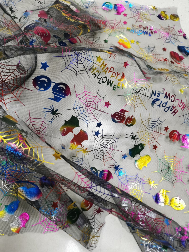 K&ouml;nnte beinhalten: Schwarzer Netzstoff mit einem regenbogenfarbenen, schillernden Druck von Spinnweben, Sternen, Geistern und dem Text "Happy Halloween".