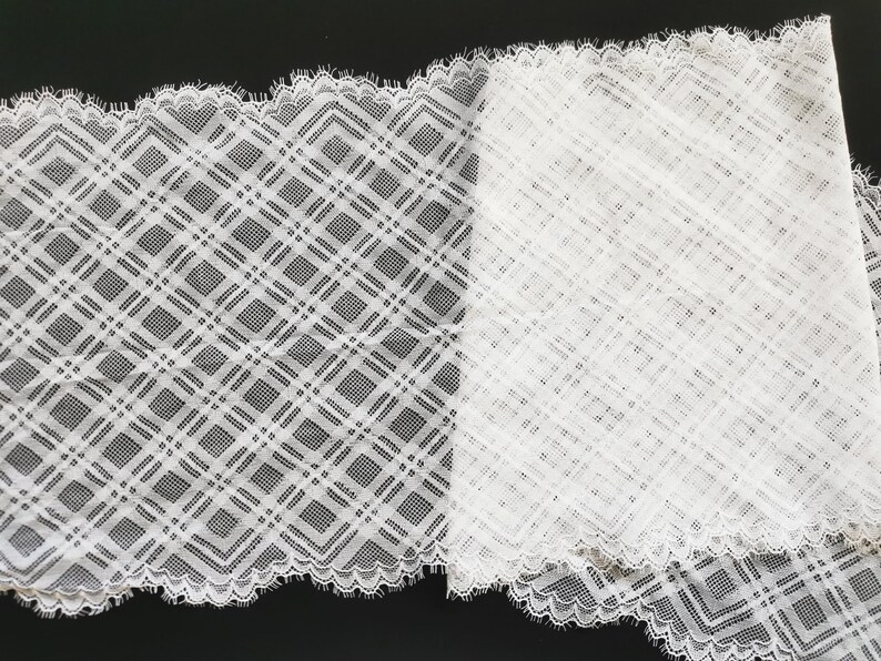 May include: White lace trim with a geometric diamond pattern. The lace has a scalloped edge.