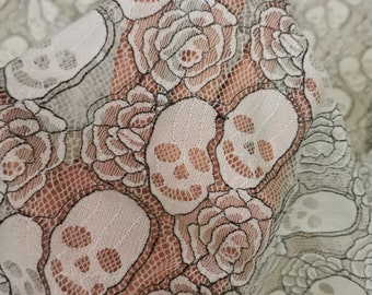 Peut inclure: Tissu en dentelle blanche avec un motif répété de crânes noirs et de roses. Le tissu est délicat et transparent.
