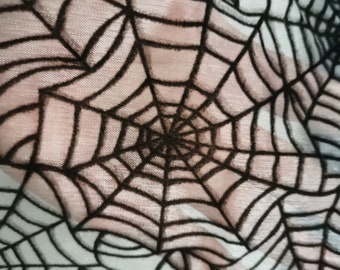 Peut inclure: Motif de toile d'araignée noire sur un tissu blanc transparent. La toile est détaillée et complexe, avec une texture légèrement duveteuse.