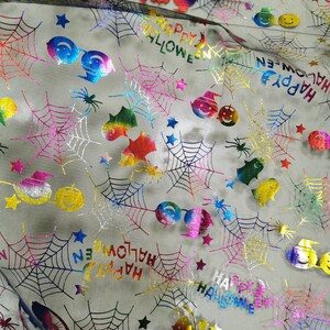 K&ouml;nnte beinhalten: Regenbogenfarbener, schimmernder Stoff mit einem schwarzen Netz&uuml;berzug. Der Stoff zeigt ein sich wiederholendes Muster aus Spinnweben, Sternen und dem Text "Happy Halloween".